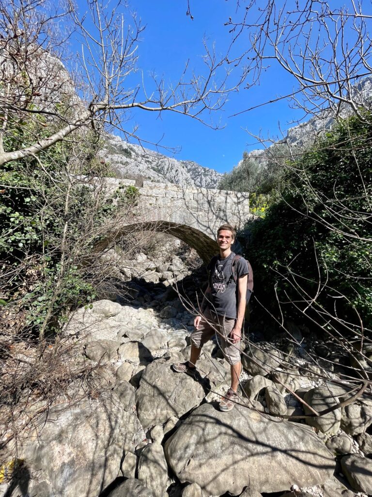 Mann steht vor mediterraner Steinbrücke